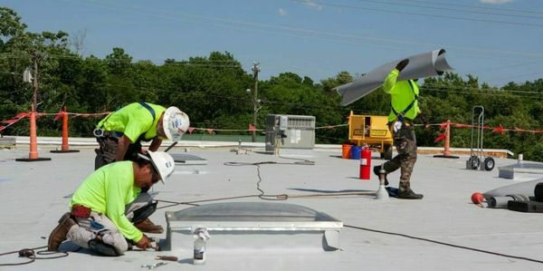 Construction workers in bright safety gear working on a rooftop under clear skies.