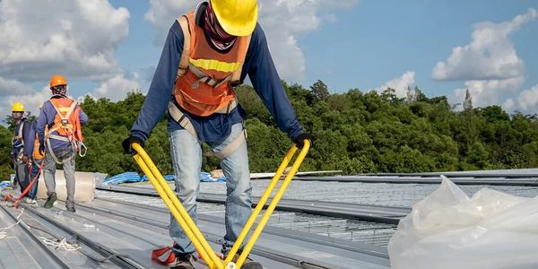 Construction workers in safety gear working on a metal roof under a partly cloudy sky.
