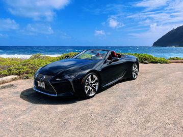 Black Lexus convertible by the ocean on a sunny day.