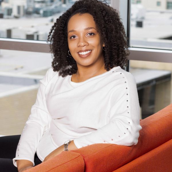 Young woman with curly hair smiling while sitting on an orange couch.