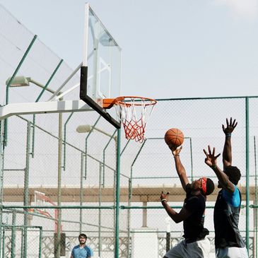 Two men playing basketball outdoors, one attempting a layup.