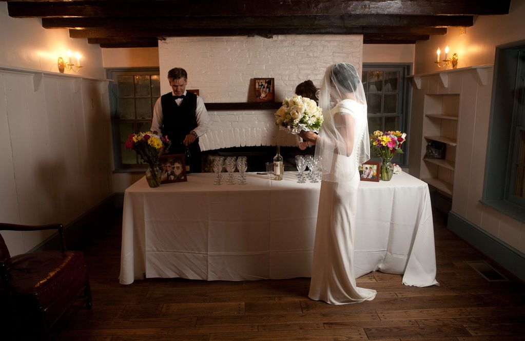 catering bartender setting up a drink station while a bride in a white gown and veil watches
