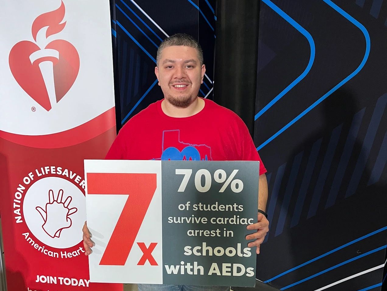 Man holding a sign about cardiac arrest survival in schools with AEDs.