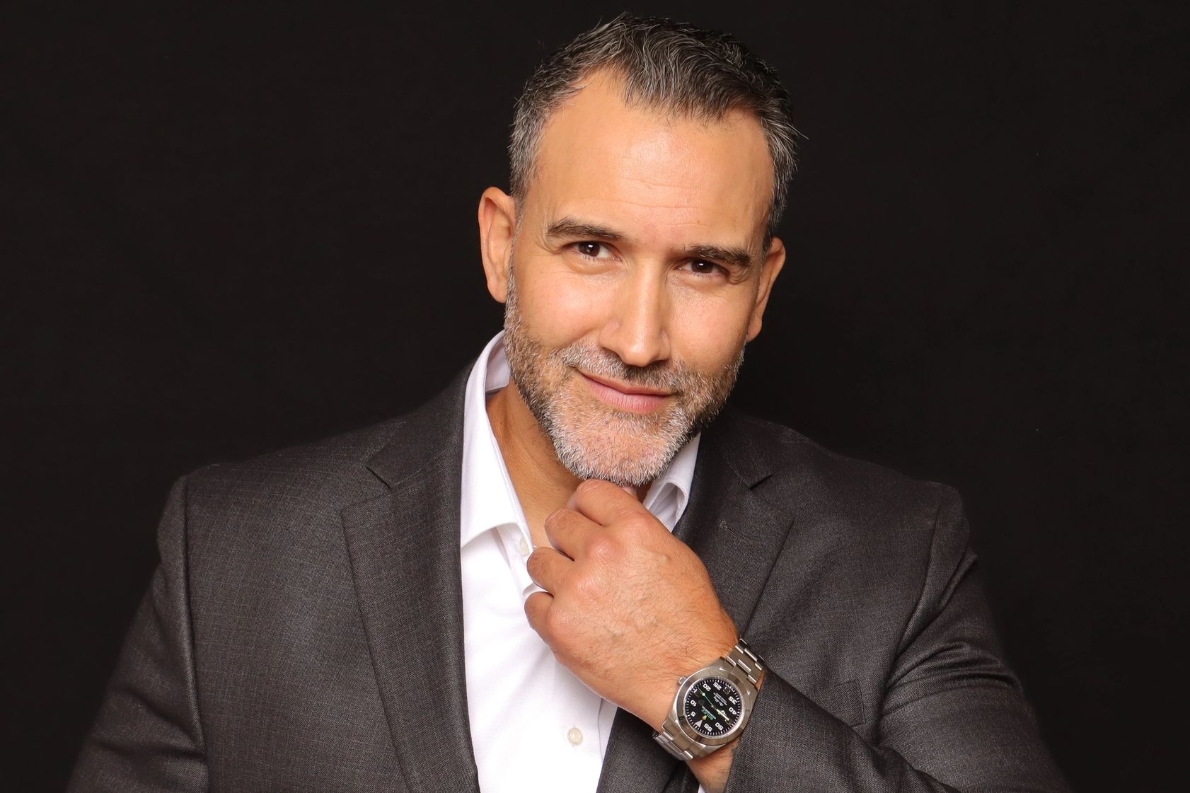Confident man in a suit with a thoughtful smile and hand on chin.