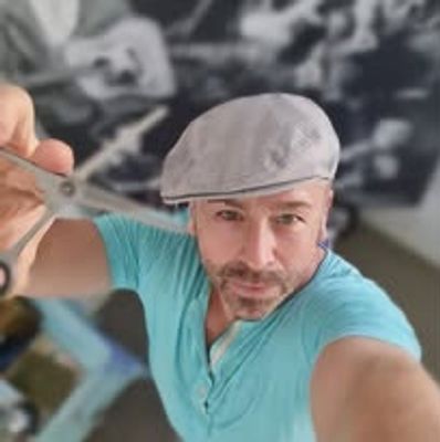 Man wearing a flat cap holding scissors towards the camera.