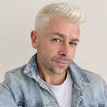 Man with platinum blonde hair wearing a denim jacket and white shirt.