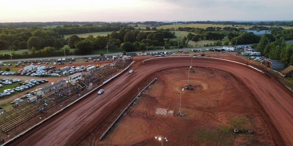 Aerial view of a dirt race track with cars and spectators.