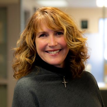 Smiling woman with curly hair and a cross necklace.