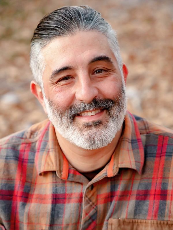 Smiling man with gray beard wearing a plaid shirt.