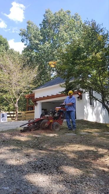 Man using a stump grinder near a white house on a sunny day.