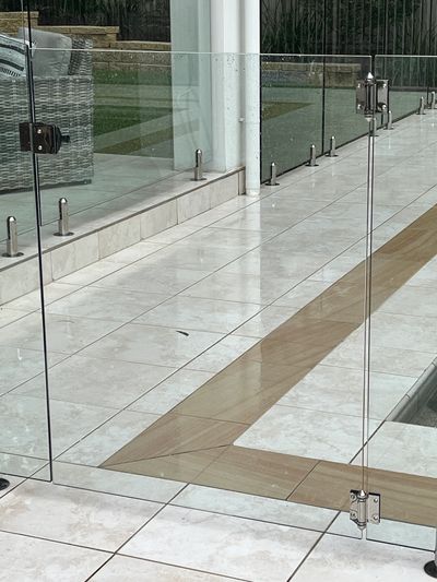 Transparent glass pool fence with metal hinges and clean tiled flooring.