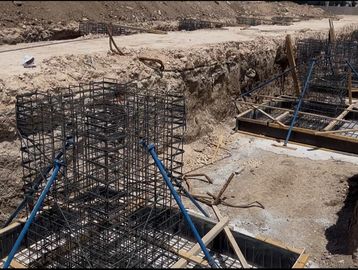 Steel reinforcement cages being set up at a construction site foundation.