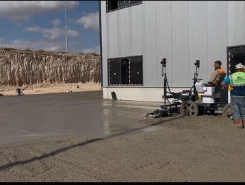 Workers use machinery to smooth freshly poured concrete outside a building.