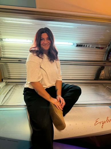 A woman sits smiling on a tanning bed inside a studio.
