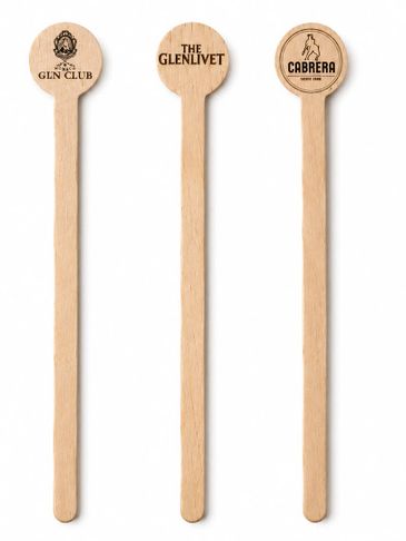 Three wooden cocktail stirrers with brand logos on top.