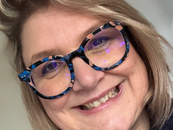 Smiling woman wearing stylish blue and pink patterned glasses.