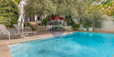 Sunny backyard with a clear swimming pool and lounge chairs under trees.