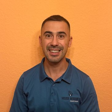 Smiling handyman in blue shirt stands against orange wall.