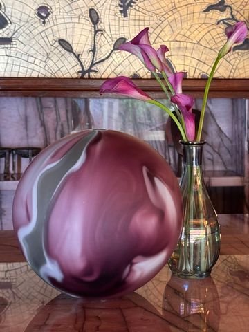 Decorative marbled orb and glass vase with purple calla lilies on a reflective table.