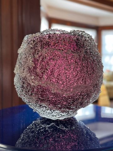A textured, translucent purple glass sphere reflecting on a shiny surface.