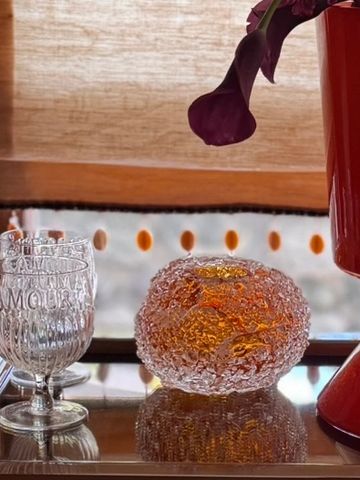 Decorative glass items and a purple flower in a red vase on a reflective surface.