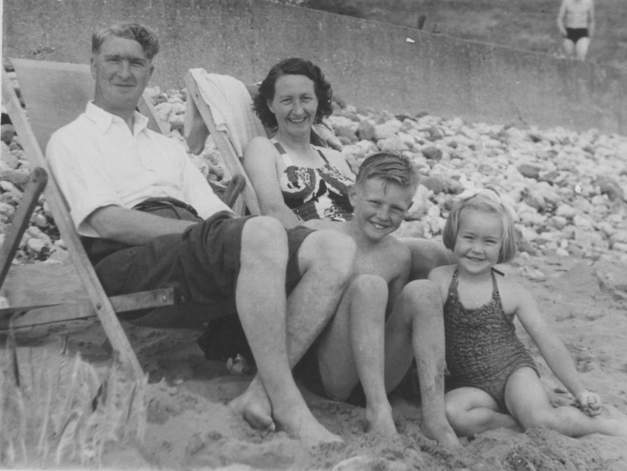 A vintage black-and-white photo of a family relaxing on a rocky beach.