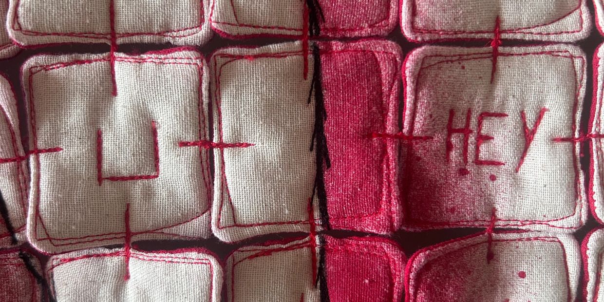 Close-up of stitched fabric squares with red patterns and arrows on a pink background.