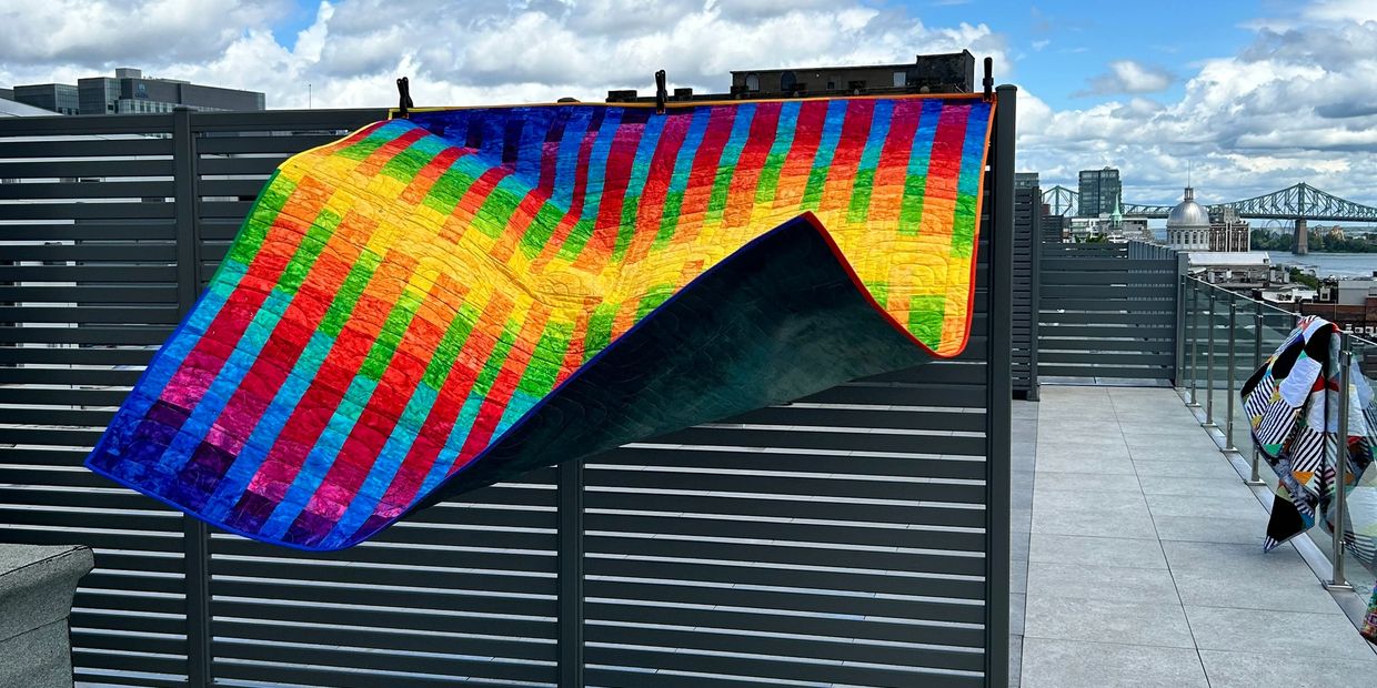 Colorful quilt hanging outdoors on a fence.