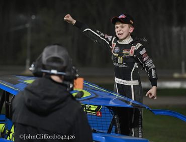 Young race car driver celebrates victory beside his vehicle at night.