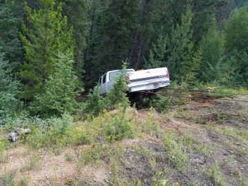 White pickup truck stuck off-road in forest.