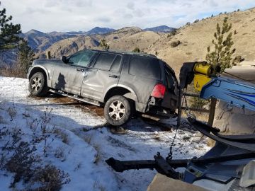 Damaged SUV being towed from snowy hill.