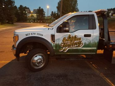 A white tow truck with green accents parked at dusk.
