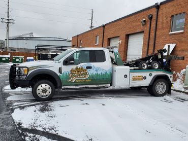 A tow truck parked in a snowy lot beside a brick building.