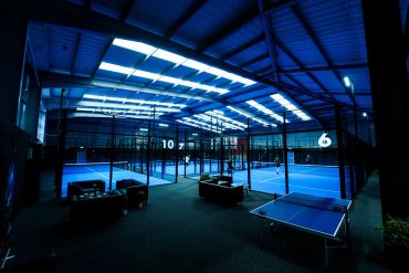 Indoor blue paddle tennis courts with seating and table tennis.