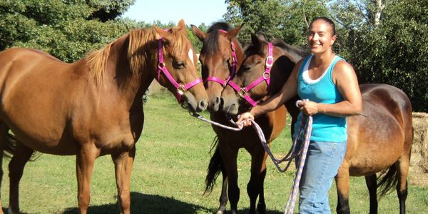 Woman smiling with three horses on a sunny day.