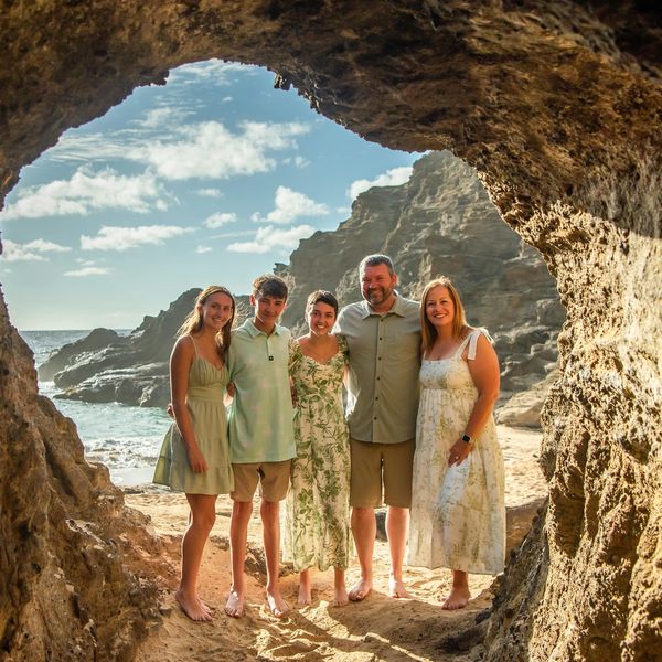 Family of five posing inside a beach cave with rocky cliffs and ocean in background.
