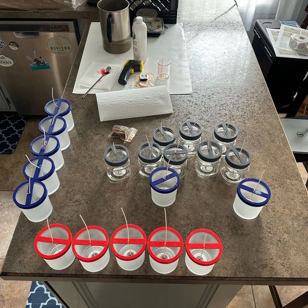 Multiple jars with colored lids and wicks placed on a kitchen counter.