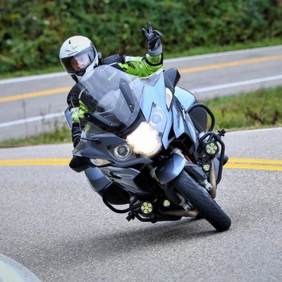 Motorcyclist making a peace sign while riding on a curved road.
