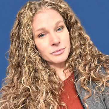 Woman with long curly blonde hair against blue background.