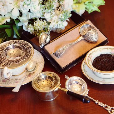 Elegant silver tea strainers with vintage teacups and floral arrangement.