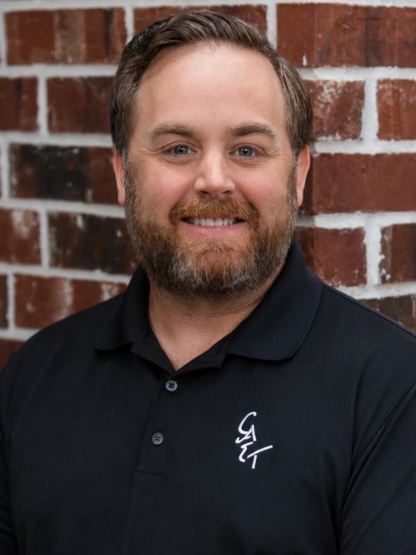 Man smiling in front of a brick wall.