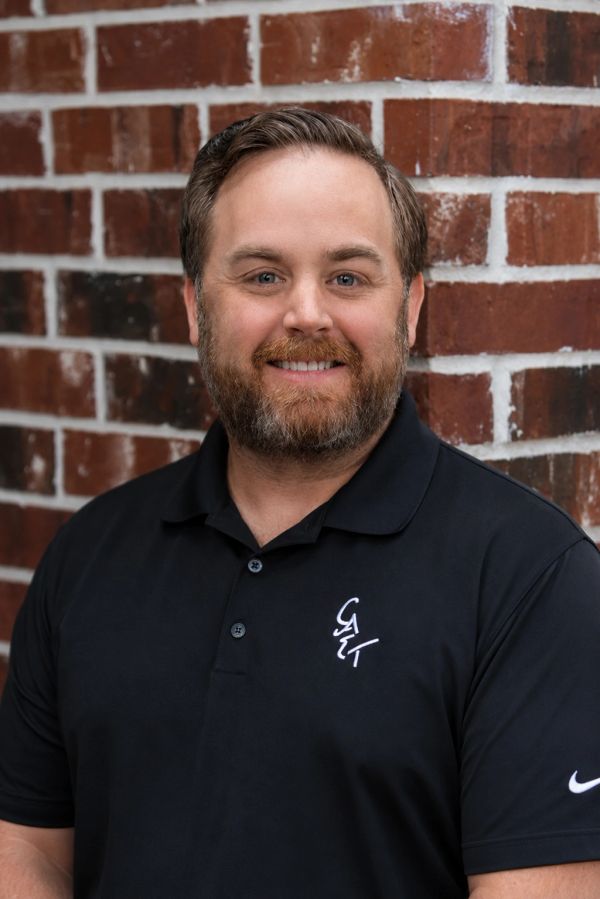 Man smiling in front of a brick wall.