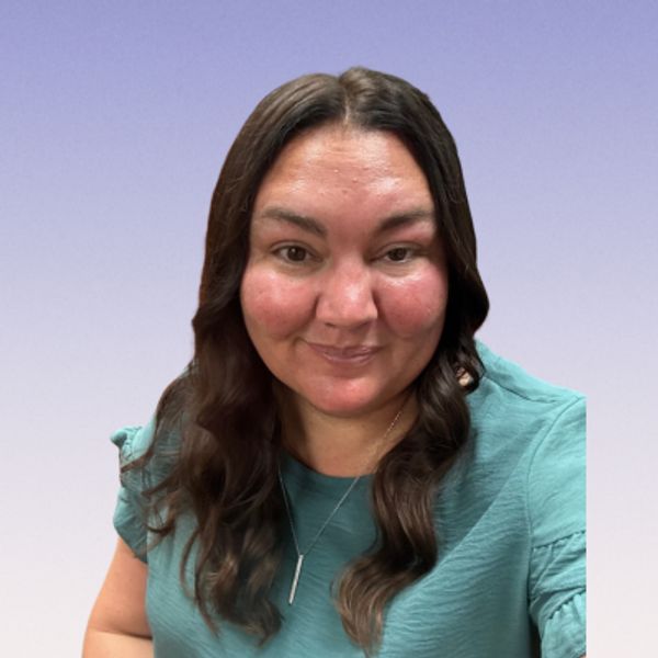 A woman with long dark hair wearing a teal shirt smiles gently.