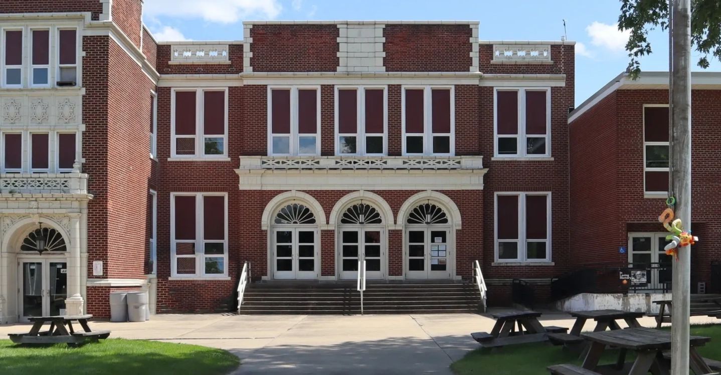 Brick school building entrance with arched doors and multiple windows.