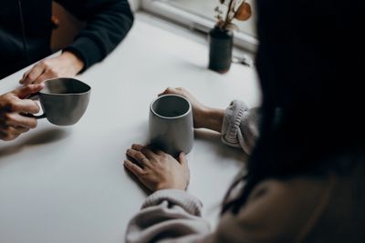 Two people sitting at a table holding mugs, engaged in conversation.