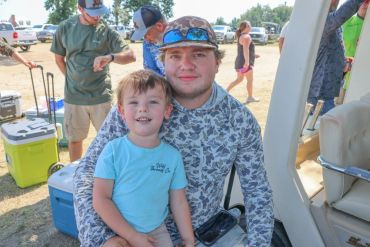 Man and child smiling outdoors near boats.