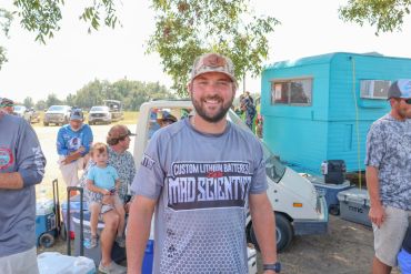 Man smiling at an outdoor event with a blue camper in the background.