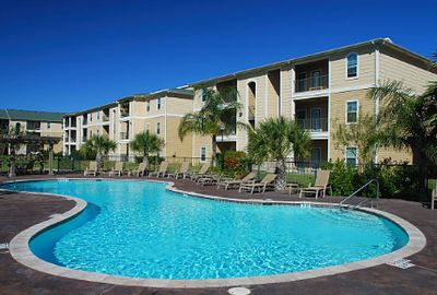 Sunny outdoor pool area with lounge chairs beside apartment buildings.