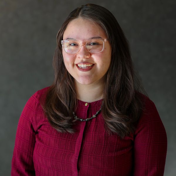 Young woman with glasses smiling against a dark background.