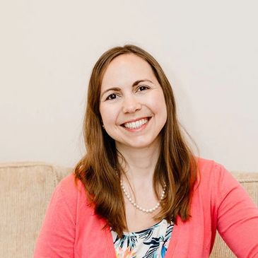 Smiling woman wearing a pink cardigan and pearl necklace.